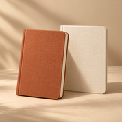 one terracotta linen-covered notebook with rounded corners and cream pages, beside a closed cream notebook, elegant stationery still life