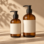 two amber glass hand-wash pump bottles, one small 250ml and one larger 500ml, matte black pumps and blank cream labels, no letters