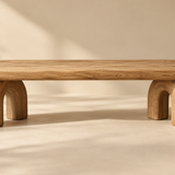 one low sculptural solid oak bench with rounded pill-shaped seat and thick arch legs, full product in wide landscape composition